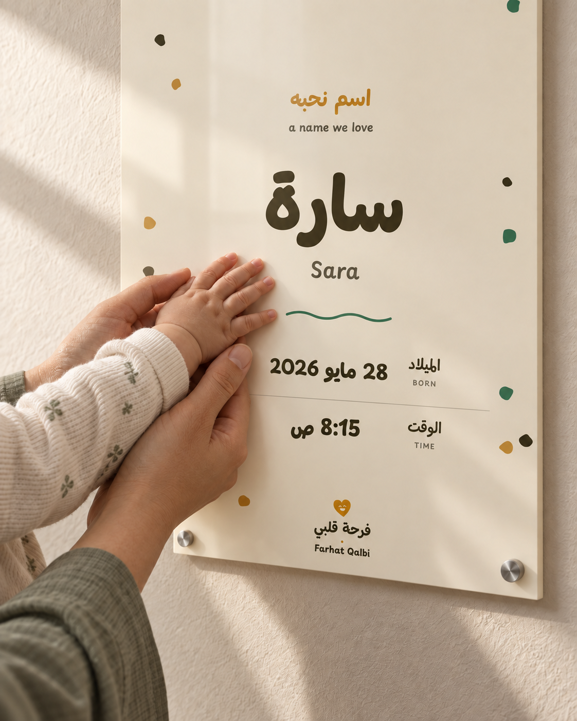 Parent and baby hands beside a personalised Arabic A Name We Love acrylic birth print in Wheat